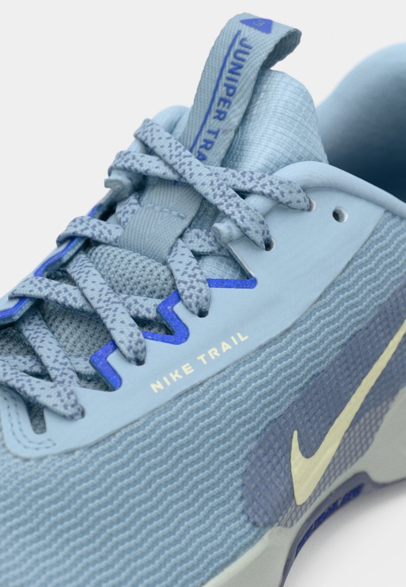 Acercamiento a una zapatilla de trail running Nike de color azul claro, con cordones estampados y el logo de Nike en blanco.