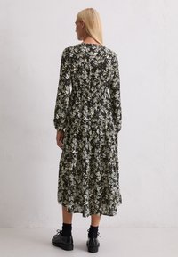 Czarna sukienka w kwiaty z długimi rękawami, dopasowaną talią, warstwową spódnicą i żywymi białymi oraz żółtymi nadrukami. Uzupełniona o czarne masywne buty.