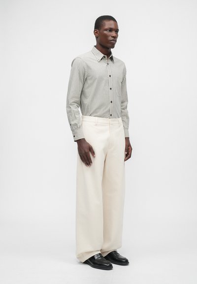 Rutet knappeskjorte i lysegrønn og hvit; kombinert med vide kremfargede bukser og svarte loafers. Glatt tekstur.