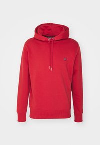 Sudadera roja hecha de una tela suave. Cuenta con un bolsillo canguro, capucha ajustable con cordón y un pequeño logo en el pecho. Puños acanalados.
