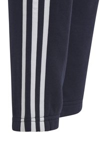 Los pantalones deportivos azul oscuro presentan rayas blancas a lo largo de los lados, están hechos de una tela suave con puños elásticos en los tobillos para un ajuste entallado.