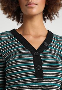 Teal and black striped top with a soft texture, featuring a V-shaped neckline and three black buttons along the front for closure.