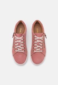 Baskets en cuir rose avec une texture lisse, présentant un design à lacets, un détail de zip argenté et des semelles intérieures beiges. Forme de pointe arrondie.