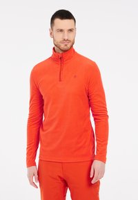 Pullover in pile di colore arancione brillante con colletto a metà zip, maniche lunghe e un piccolo logo sul petto. Tessuto morbido e vestibilità rilassata.