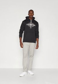 Sweatshirt preta com capuz e logótipo "CHAMPION", combinada com calças de treino cinza claro e sapatos brancos. Tecido suave e corte descontraído.