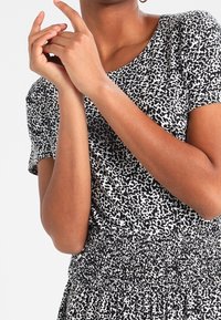 Krátký rukáv top v černobílém zvířecím motivu; měkká, pružná tkanina s volnějším střihem; viditelný smockovaný detail na pase.