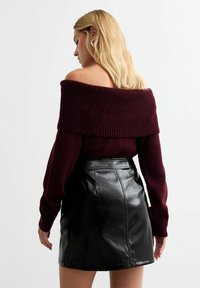 Suéter burdeos off-the-shoulder con cuello acanalado, combinado con una minifalda de cuero negro brillante. Textura suave, diseño ajustado.
