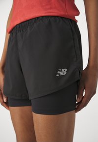 Black athletic shorts with an elastic waistband, featuring a lightweight texture and a reflective logo on the side. Layered design for comfort.