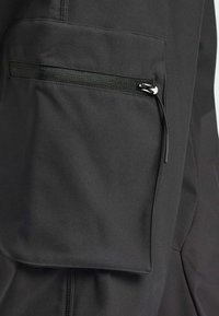Zwarte buitenkleding met een ritszak, gemaakt van gladde, textuurstof. Kenmerkend zijn de nauwkeurige stiksels en het slanke ontwerp.