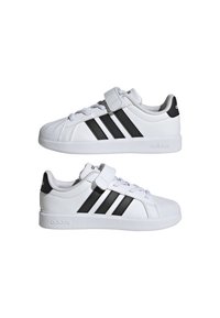 Baskets blanches à surface lisse, avec trois bandes diagonales noires, une bride en Velcro et une semelle en caoutchouc. Design à coupe basse.