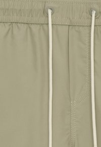 Shorts beige clair avec une taille élastique, dotés d'un cordon de serrage et d'une poche avant avec un subtil détail de couture. Texture lisse.
