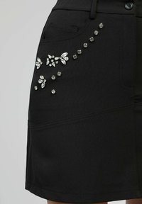Jupe noire avec poche avant décorée de strass clairs dispersés et regroupés en motifs floraux.