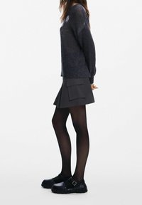 Pull en maille bleu marine à coupe décontractée, associé à une jupe plissée charbon avec une grande poche, et des sandales noires épaisses.