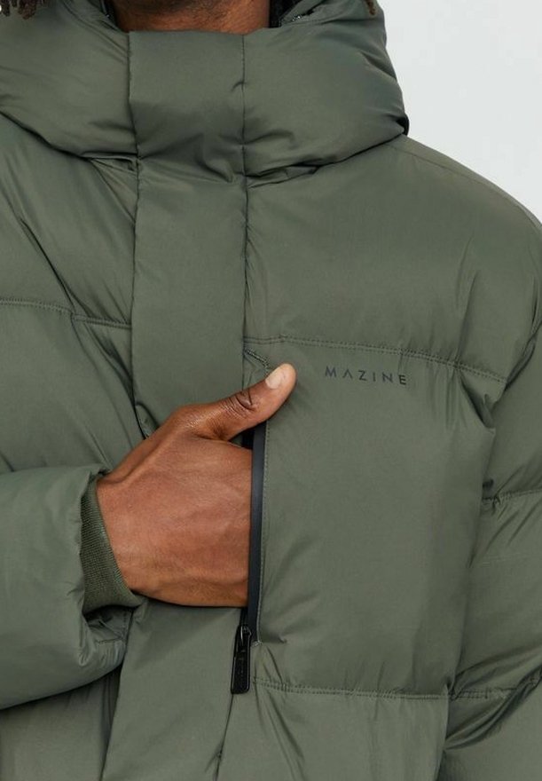 Mano cerrando la cremallera del bolsillo en el pecho de una chaqueta acolchada verde de la marca Mazine con cuello alto.