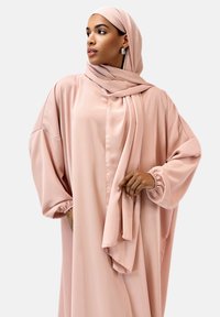 Abaya en satin rose pâle avec de longues manches amples et un hijab assorti, présentant un drapé élégant et des poignets froncés. Texture lisse, embellissements minimes.