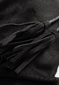 Matériau en daim noir présentant plusieurs glands texturés, chacun avec un bord doux et effilé, disposés en motifs superposés.