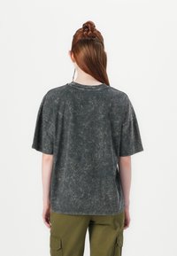 Graues, übergroßes T-Shirt mit einem verblassten, strukturierten Look. Kurze Ärmel, runder Ausschnitt und lockere Passform, kombiniert mit grünen Cargo-Hosen.