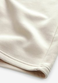 Tissu en coton beige avec une texture lisse, présentant un ourlet soigneusement cousu le long du bord et de subtiles plis drapés.