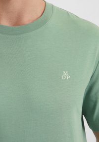 T-shirt a maniche corte di colore verde chiaro, realizzato in tessuto morbido, con un piccolo logo bianco sulla parte sinistra del petto e un classico scollo rotondo.
