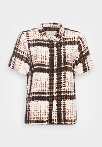 Chemise à manches courtes en crème et marron, présentant un motif en grille avec des lignes irrégulières. Le tissu est lisse ; design col avec une fermeture à boutons.