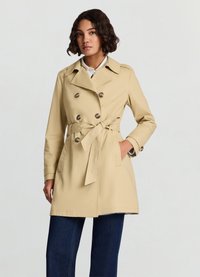 Trench-coat beige à double boutonnage avec une taille ceinturée, doté d'un col et de poches latérales. Le tissu semble lisse avec une légère brillance.