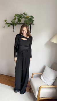 Melnas garām piedurknēm izstrādāts tops no elastīga auduma ar izgriezumu, kombinēts ar melniem augstajiem platām biksēm. Vienkāršs, minimālistisks dizains.