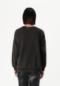 Sudadera gris oscuro con un ajuste holgado, puños y dobladillo acanalados, y cuello redondo. Textura suave y diseño minimalista visible desde atrás.