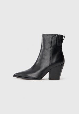 Botas de tornozelo em couro preto com bico pontudo, parte superior texturizada e salto alto grosso. Apresenta um painel elástico lateral para facilitar o calçar.