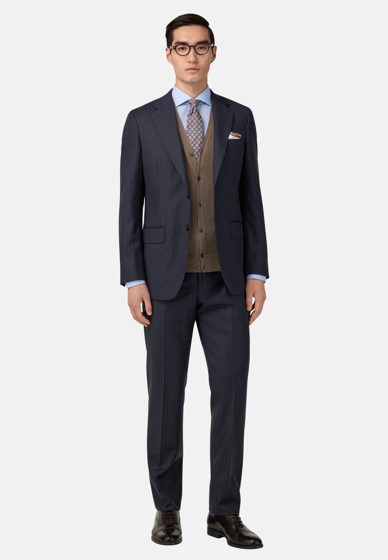 Jūras spēku uzvalks ar brūnu vestu, gaiši zilu kreklu un rakstainu kaklasaiti. Kurpes ir tumši brūnas ādas. Iespējams, kabatas lakatiņš.