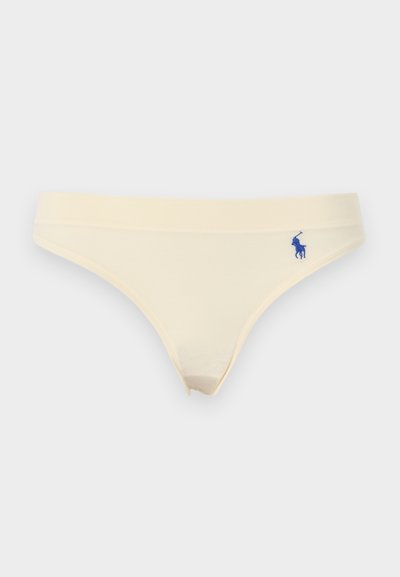 Γυναικεία μπικίνι σε κρεμ χρώμα με μικρό μπλε κεντημένο λογότυπο στο αριστερό ισχίο, σε λευκό φόντο.