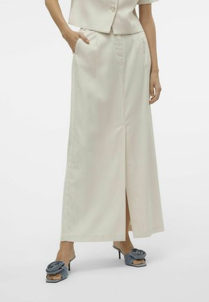 Cream-colored maxi skirt featuring a front slit, side pockets, and a smooth texture. Paired with blue heeled mules with floral accents.