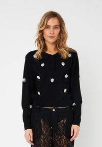 Maglione nero con colletto, decorato con applicazioni floreali argentate, abbinato a pantaloni in pizzo nero trasparente. Materiale in maglia morbida, vestibilità comoda.