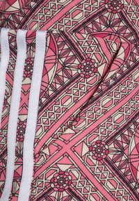 Legíny s geometrickým vzorem v růžové a krémové barvě, s černými obrysy. Obsahují tři bílé pruhy po jedné straně. Měkká textura.