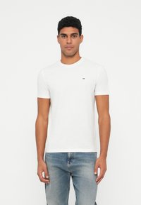 Λευκό βαμβακερό T-shirt με κοντά μανίκια, στρογγυλή λαιμόκοψη και μια μικρή λεπτομέρεια λογότυπου στο στήθος. Συνδυάζεται με ανοιχτόχρωμο μπλε τζιν.