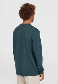 Tumedast teal'ist värvi pika varrukaga, ümarate krae ning tekstuuriga materjalist särk. Omab lõdva istuvust ja veidi langetatud õlgasid.