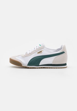 Witte en beige Puma Roma sneaker met groene streep, vetersluiting en gumzool, zijaanzicht tegen een effen achtergrond.