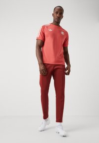 Röd idrottströja med korta ärmar och vita ränder, kombinerad med röda slim-fit byxor. Har vita logotypdetaljer och vita skor.