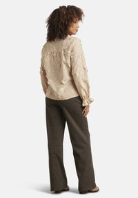 Beige blouse with floral embroidery, ruffled neckline, and long sleeves, paired with brown checkered wide-leg pants.