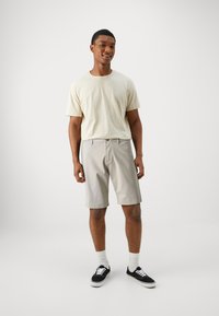 Tricou scurt de culoare bej deschis, pantaloni scurți gri deschis, șosete albe și adidași negri. Design simplu, croială lejeră și textură moale.
