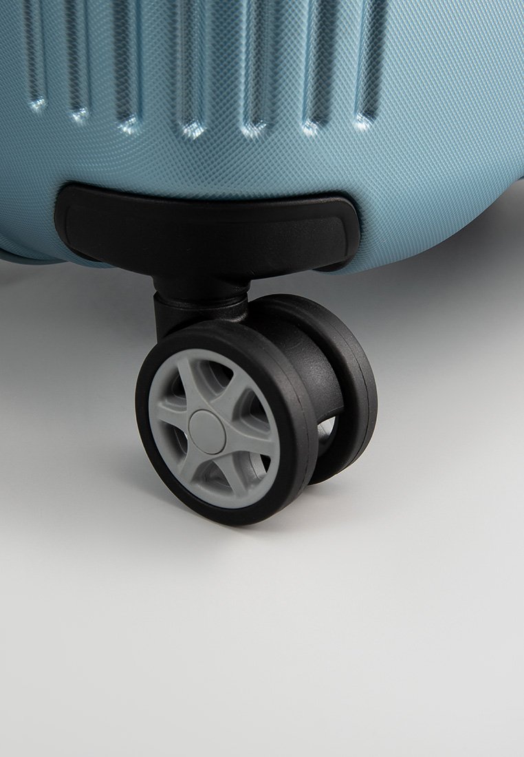 Esquina de maleta azul de carcasa dura con una estructura negra, que cuenta con dos ruedas negras con radios grises para una movilidad suave. Detalle de superficie texturizada visible.