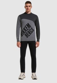 Maglione grigio e nero con un design geometrico. Presenta un colletto a girocollo, maniche lunghe e testo del logo in diagonale. Abbinato a pantaloni neri e sneakers.