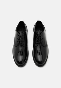 Scarpe stringate in pelle verniciata nera con una superficie liscia e lucida, punta arrotondata e dettagli cuciti lungo la suola.