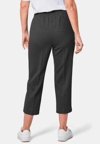 Dunkelgraue, gekürzte Hosen mit einem elastischen Bund, maßgeschneidertem Design und geripptem Muster, kombiniert mit weißen Sportschuhen.