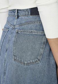 Ljusblå denimkjol med en bakficka, synliga sömmar och en väldefinierad midja. Texturen är typisk för denimtyg.