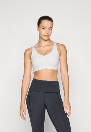 Grå sportsbh med brede stropper og V-hals, laget av mykt stoff og med et bånd under bysten. Kombinert med høy midje svarte leggings.