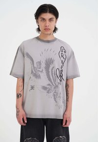 Camiseta gris de gran tamaño hecha de algodón con un estampado gráfico de dragón y águila, mangas cortas y un cuello redondo acanalado.