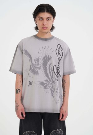T-shirt oversize gris en coton avec un motif graphique de dragon et d'aigle, manches courtes et col ras du cou côtelé.