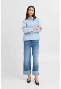 Svetle modrá košilová košile s pruhy a límečkem, spárovaná se širokými džíny s třepenými lemy a černými lodičkami s špičatou špičkou.