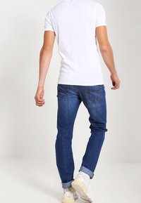 Vitt kortärmat skjorta kombinerat med blå jeans, som visar en smal passform, upprullade ärmar och synlig söm på bakfickorna. Avslappnad stil.