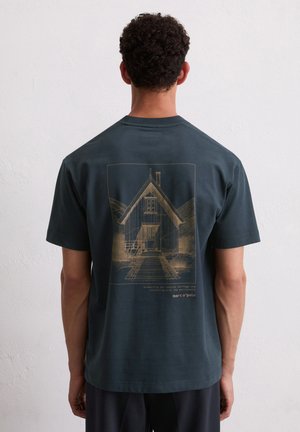 Donkerblauwe t-shirt met korte mouwen, voorzien van een gouden illustratie van een huis, met tekst die milieubewustzijn promoot en de merknaam.